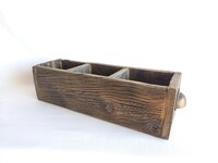 May include: A rectangular, dark brown wooden box featuring a weathered, textured grain and a prominent knot on the front panel. The interior is divided into three separate compartments by two wooden partitions, and a small metal handle is visible.