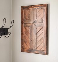 May include: A rectangular wall art piece constructed from dark stained wooden planks arranged in a geometric pattern to form a central cross shape. The wood features visible grain and knots, framed by a solid dark wood border with a smooth finish.