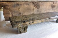 May include: A rectangular wooden riser featuring a dark, weathered finish with visible wood grain, knots, and a rough, textured surface. The piece is supported by two sturdy, matching wooden legs, showcasing a natural, aged appearance throughout.
