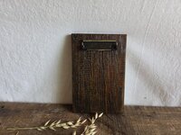 May include: A rectangular clipboard made of dark brown stained wood with a prominent vertical grain texture. The top of the board features a metallic, antique brass-colored spring-loaded clip mechanism secured with two small black screws.
