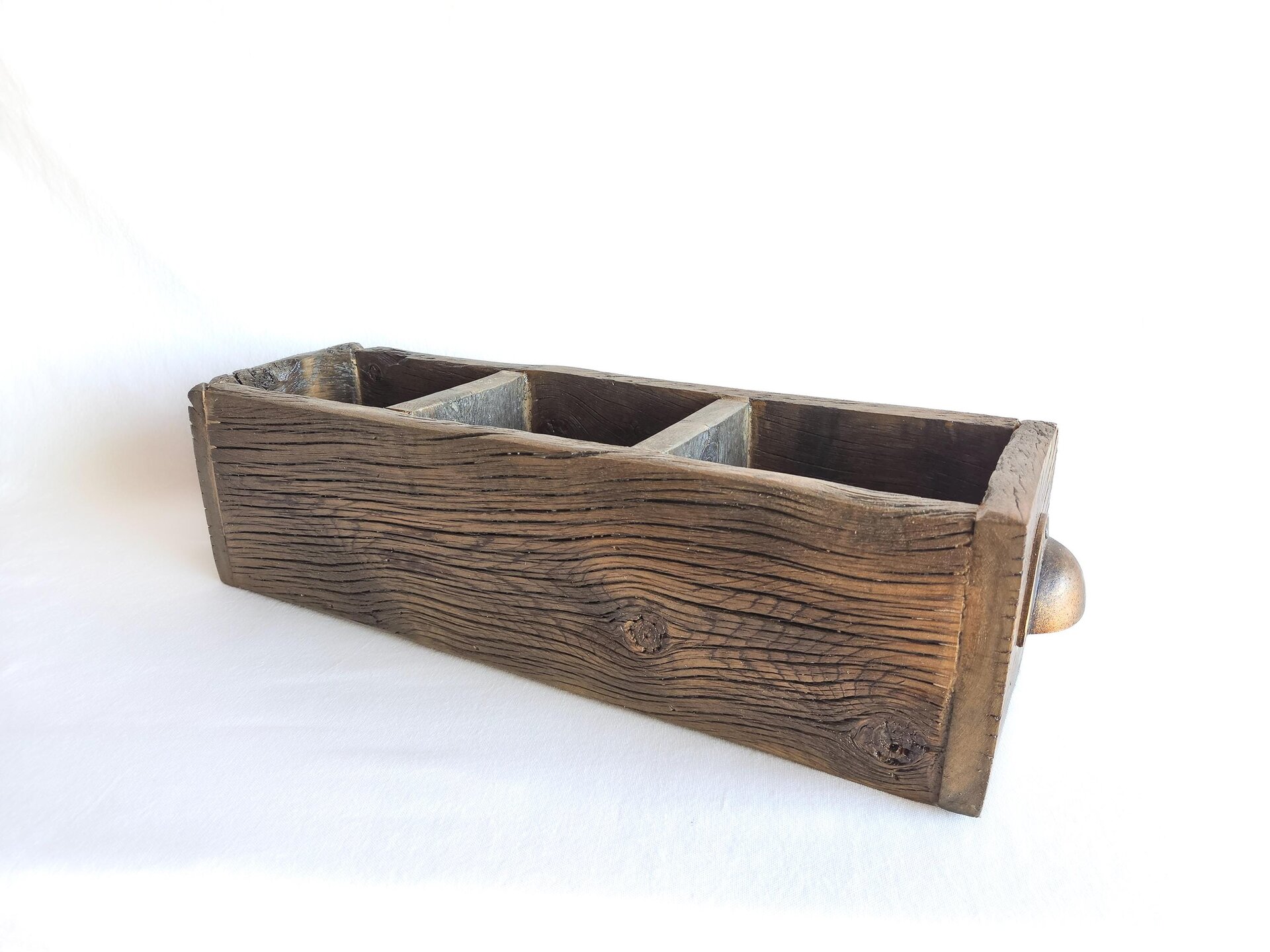 May include: A rectangular, dark brown wooden box featuring a weathered, textured grain and a prominent knot on the front panel. The interior is divided into three separate compartments by two wooden partitions, and a small metal handle is visible.