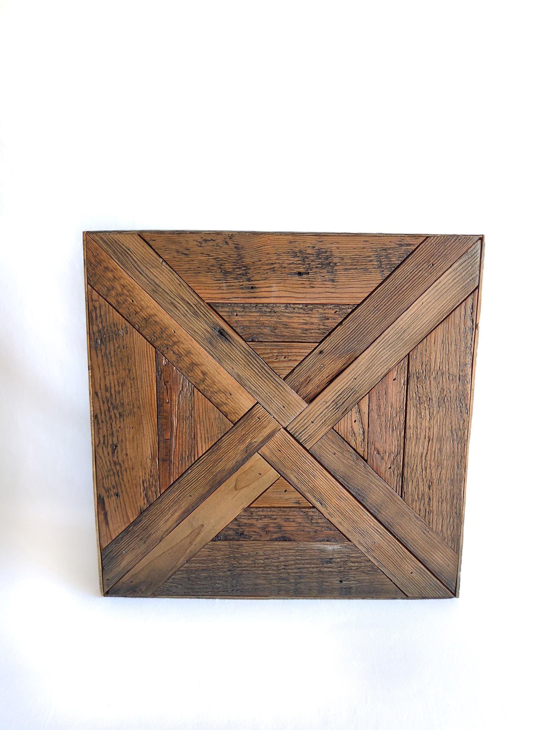 May include: A square wooden wall art piece constructed from reclaimed planks arranged in a geometric pattern. The design features two intersecting diagonal strips forming an X shape, surrounded by vertical and horizontal wood grain textures.