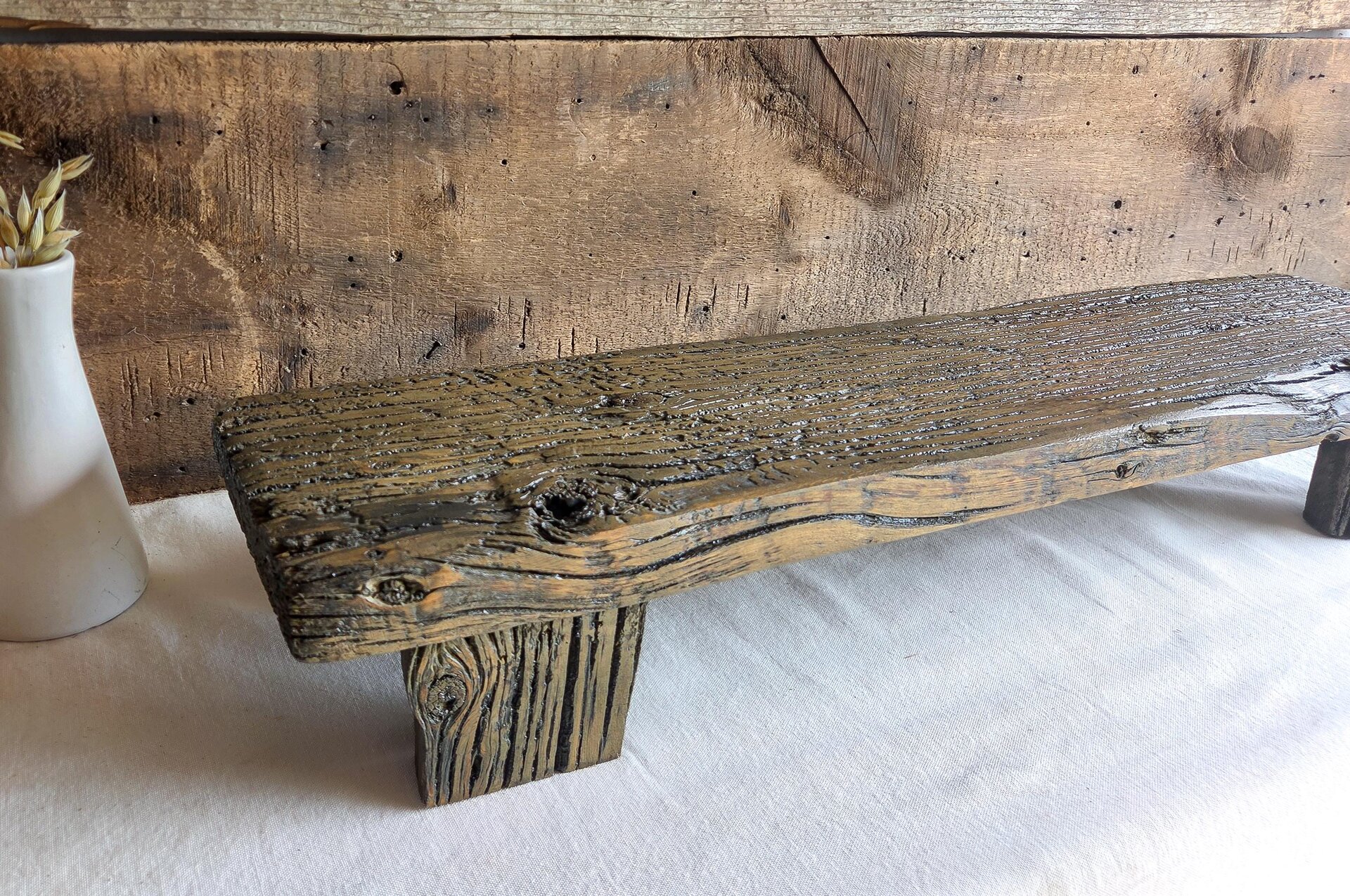 May include: A rectangular wooden riser featuring a dark, weathered finish with visible wood grain, knots, and a rough, textured surface. The piece is supported by two sturdy, matching wooden legs, showcasing a natural, aged appearance throughout.