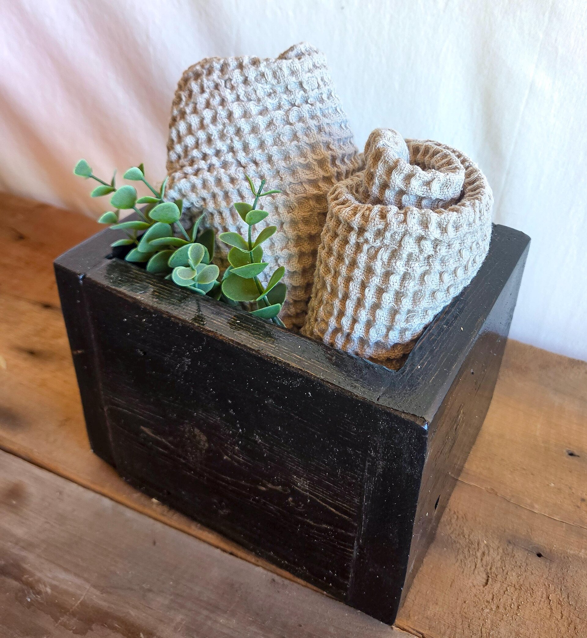 Handmade rustic wooden organizer caddy crafted from reclaimed wood, styled with rolled washcloths and greenery for farmhouse bathroom countertop storage.