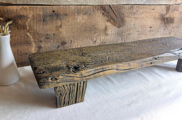 May include: A rectangular wooden riser featuring a dark, weathered finish with visible wood grain, knots, and a rough, textured surface. The piece is supported by two sturdy, matching wooden legs, showcasing a natural, aged appearance throughout.