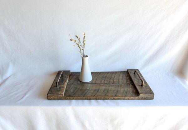 May include: A rectangular wooden serving tray with a dark brown stained finish and visible wood grain texture. The tray features two metallic handles on the sides and holds a small, plain white ceramic vase containing a few dried oat stalks.